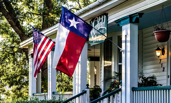 The Texas and United States flags hang proudly from the porch of a home, expressing a deep love for Texas.
