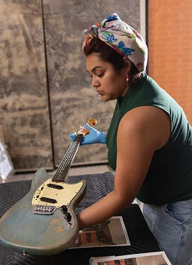 Veronique Medrano carefully cleans a guitar, reflecting her work as an archivist preserving Tejano music heritage.