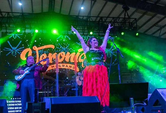 Veronique Medrano sings joyfully on a brightly lit stage with her band, celebrating her musical heritage as a superstar.