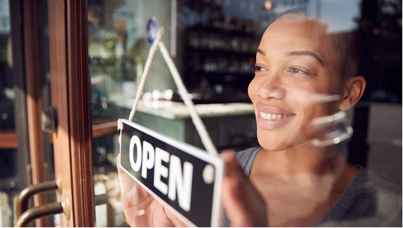 A woman smiling behind an open sign.
