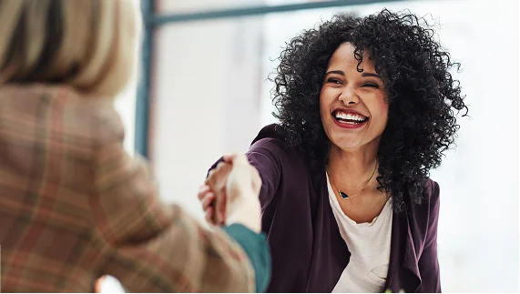 A smiling woman in a professional setting shakes hands with a colleague, symbolizing a veteran's successful career transition.